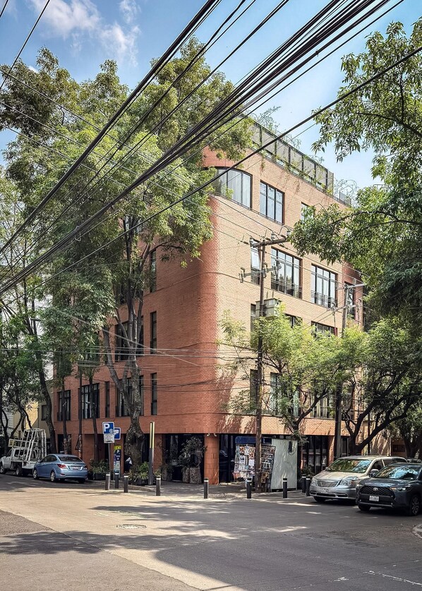 A multi-story building with a brick facade, large windows, and a parking sign. - EMA Condesa (Mexico City)