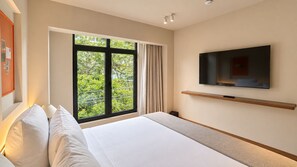 Une chambre d’hôtel avec un grand lit, un téléviseur fixé au mur et une fenêtre donnant sur un paysage verdoyant.