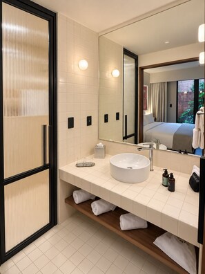 A modern bathroom with a large mirror, white tiles, a round sink, and a wooden shelf with towels. - EMA Condesa (Mexico City)