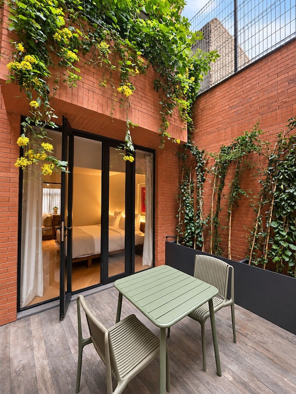 A room with a bed, a table, and chairs, a sliding glass door, and a brick wall with climbing plants. - EMA Condesa (Mexico City)
