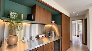 A modern kitchen with a stainless steel countertop, wooden cabinets, and a potted plant. - EMA Condesa (Mexico City)