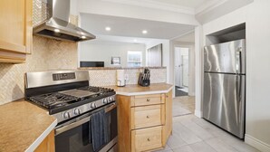 Eine moderne Küche mit Edelstahlherd, -backofen und -kühlschrank, Holzschränken und einer gefliesten Spritzschutzwand.
