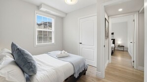 Ein Schlafzimmer mit Bett, einem Fenster mit Jalousien, einer Tür und einem Flur, der in einen anderen Raum führt.