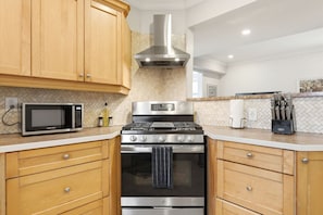 A kitchen with wooden cabinets, a stainless steel range hood, a microwave, a stove, and a knife block. - Main Floor 2BR Retreat, 2 Parking, 1 Bath & Wi-Fi (Pickering)