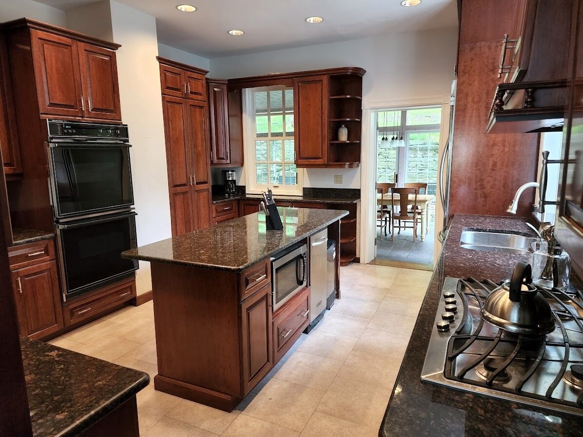 A kitchen with dark wooden cabinets, a granite countertop, a built-in oven, a stove, and a window providing natural light.