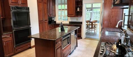 A kitchen with dark wooden cabinets, a granite countertop, a built-in oven, a stove, and a window providing natural light.