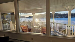 Eine überdachte Terrasse mit Blick auf einen See, Holzstühle und ein Tisch.