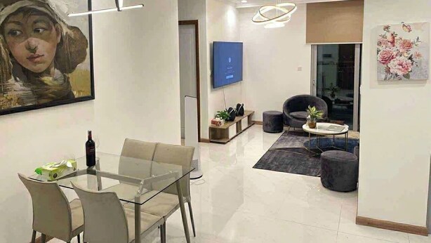 A modern living room with a glass dining table, a sofa, and a TV mounted on the wall. - Vinhomes central park  (Ho Chi Minh City)