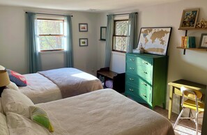 Une chambre avec deux lits, une commode verte, un bureau et une chaise.