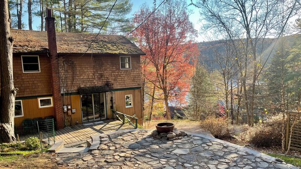 A rustic cabin with a stone-paved entrance, a chimney, and a wooden deck. - A conscious retreat overlooking the Delaware River (Beach Lake)
