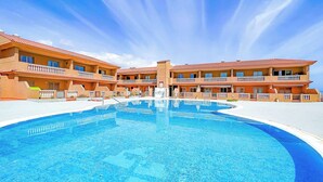 Un hotel con una piscina grande, varios balcones y un cielo azul despejado.