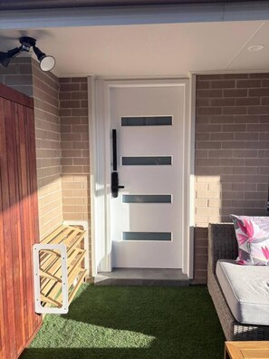 A room with a white door, artificial grass, a wicker chair, and a small wooden table.