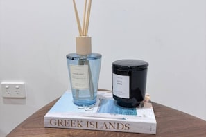 Ein Buch mit dem Titel 'Greek Islands' auf einem Holztisch, zusammen mit einer blauen Flasche und einer schwarzen Kerze.