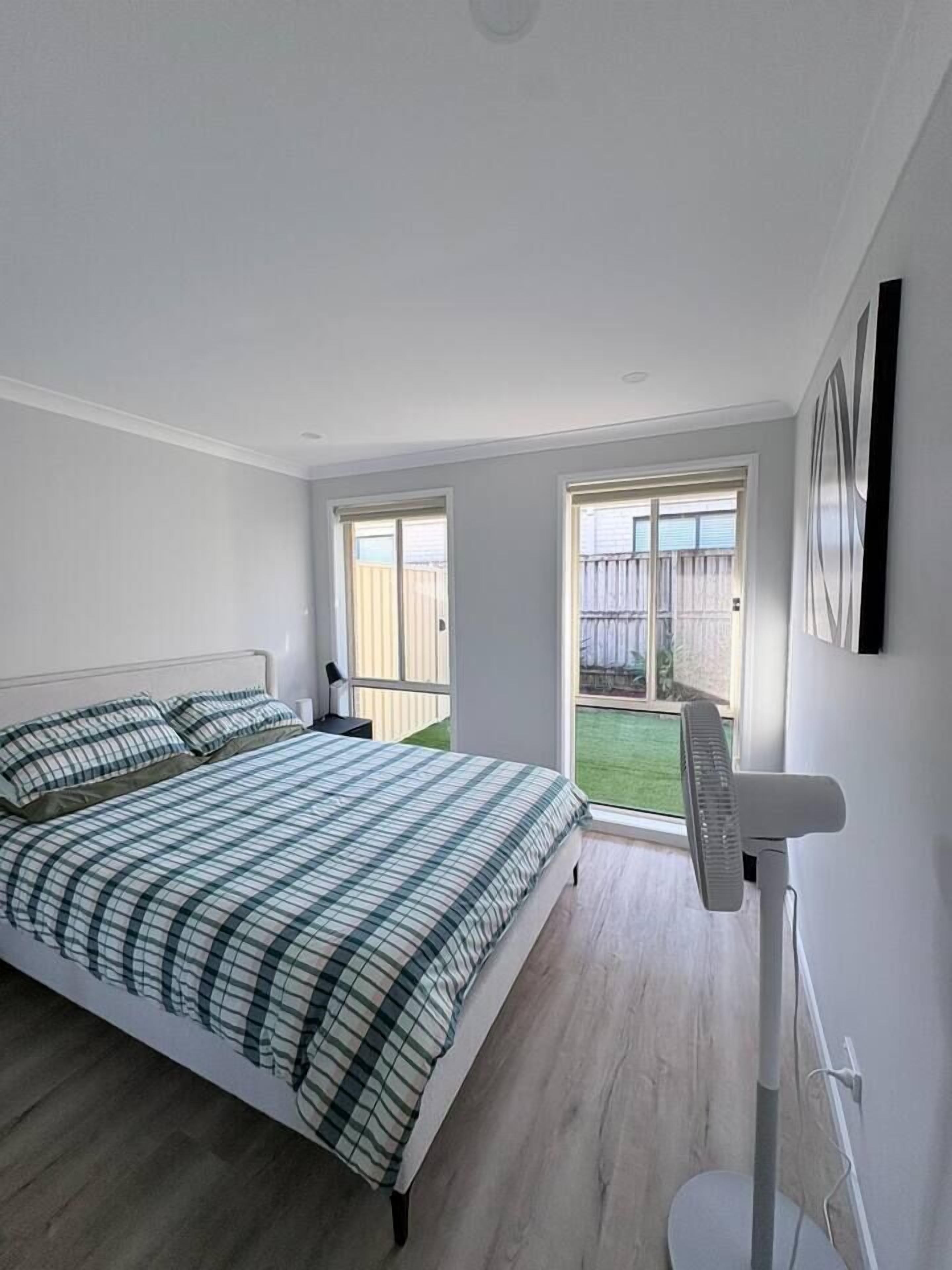 A bedroom with a bed, a standing fan, and a sliding glass door leading to a balcony.