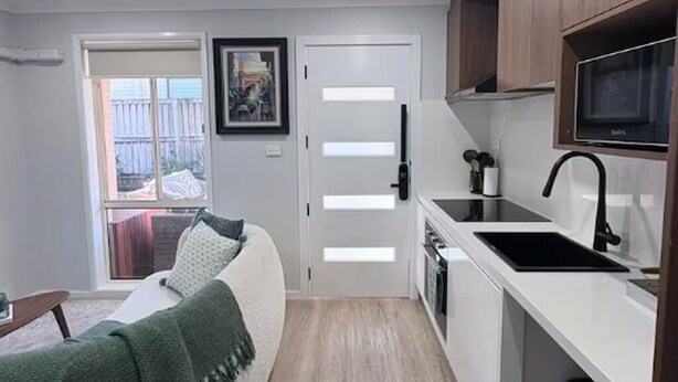 A compact kitchen with a white countertop, black sink, and wooden cabinets.