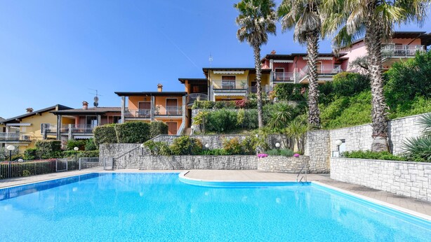 A swimming pool with a stone wall and a stone staircase leading to a building with balconies. - MGH- Garda Hills Family Stay (Polpenazze del Garda)