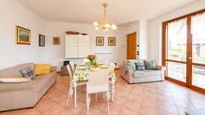 A living room with a dining table, two sofas, a chandelier, and a large window. - MGH- Garda Hills Family Stay (Polpenazze del Garda)