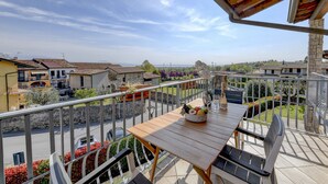 A balcony with a wooden table, chairs, and a bowl of fruit. - MGH- Garda Hills Family Stay (Polpenazze del Garda)