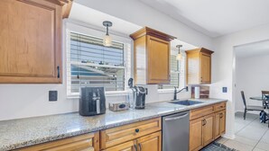 A modern kitchen with granite countertops, wooden cabinets, a dishwasher, and a window with blinds. - Relaxing Stay Minutes from the beach (Seminole)