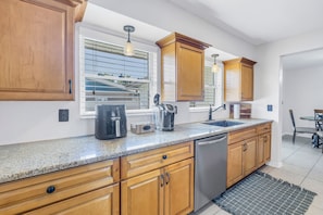 A modern kitchen with granite countertops, wooden cabinets, a dishwasher, and a window with blinds. - Relaxing Stay Minutes from the beach (Seminole)