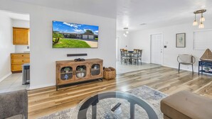 A modern living room with a flat-screen TV, wooden cabinet, and a dining area with chairs and a table. - Relaxing Stay Minutes from the beach (Seminole)