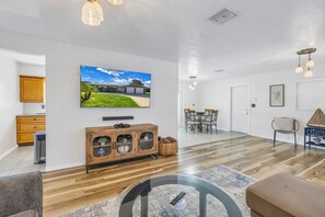 A modern living room with a flat-screen TV, wooden cabinet, and a dining area with chairs and a table. - Relaxing Stay Minutes from the beach (Seminole)