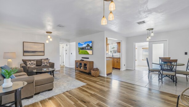 A spacious living room with a sofa, coffee table, and TV, wooden flooring, and a dining area with a table and chairs. - Relaxing Stay Minutes from the beach (Seminole)