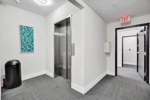 A modern elevator, a fire extinguisher, and an exit sign in a hallway.