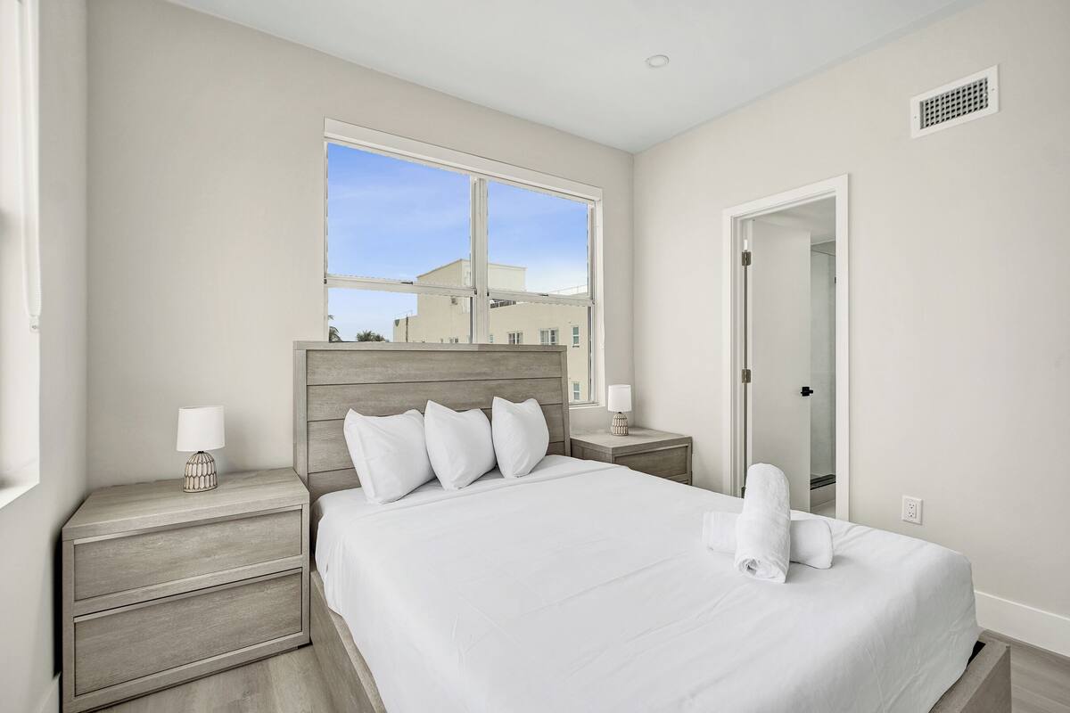 A hotel room with a large bed, a nightstand, a bedside table, a window, and a door.