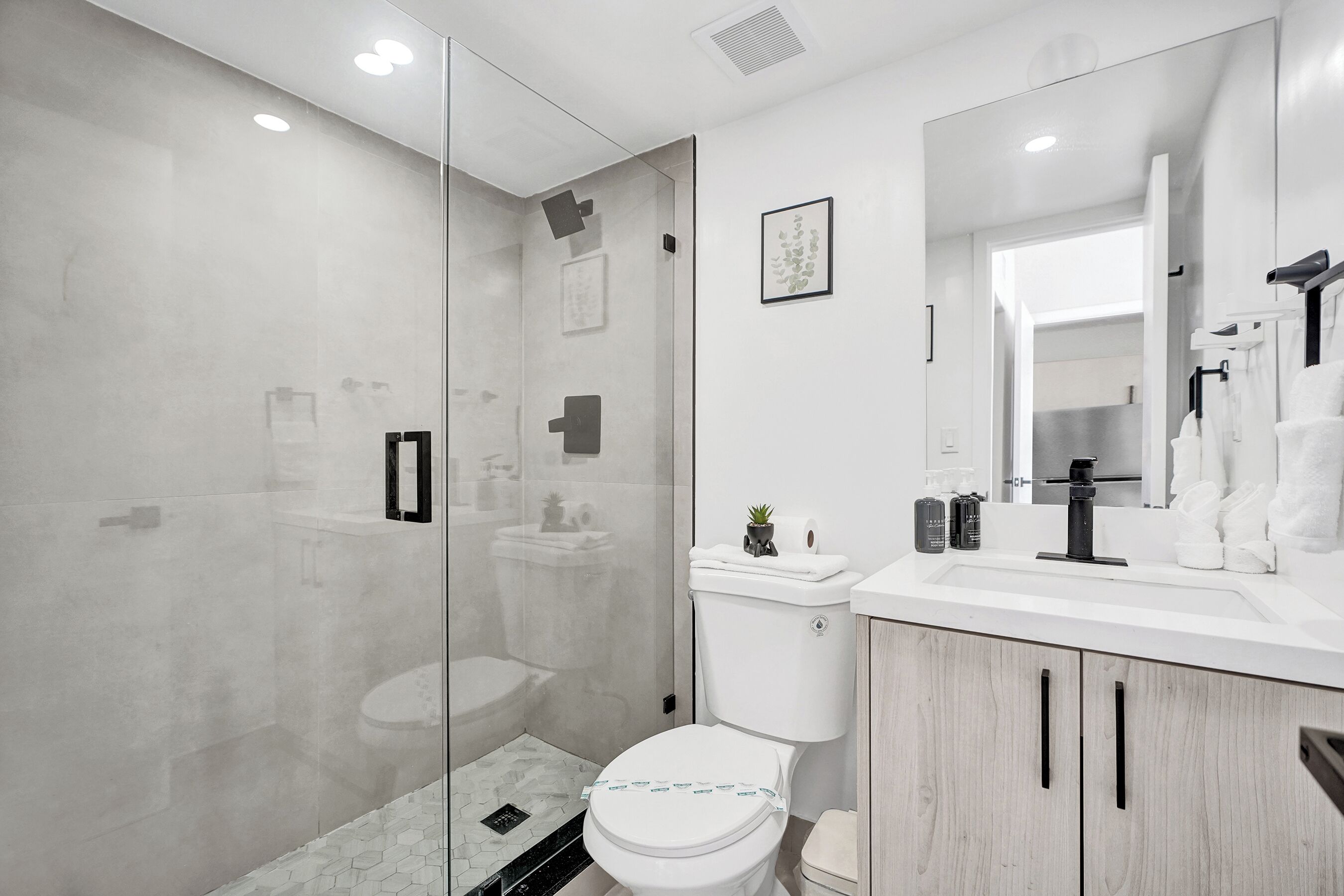 A modern bathroom with a glass shower enclosure, a white toilet, a sink with a mirror, and wooden cabinets.