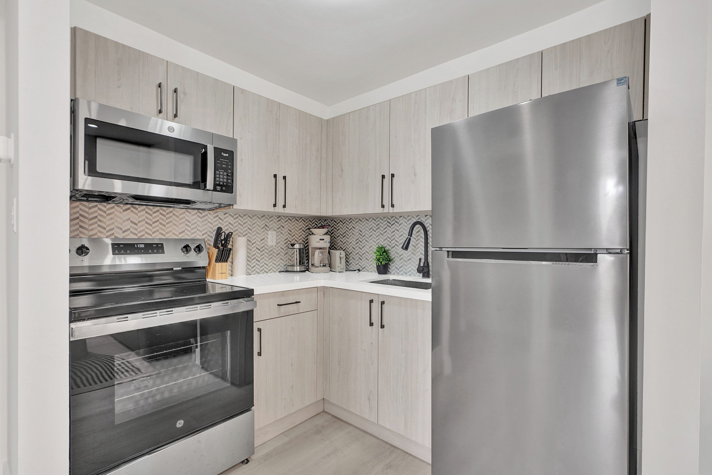 Een moderne keuken met roestvrijstalen apparatuur, licht houten keukenkastjes en een backsplash met een herringbone-patroon.