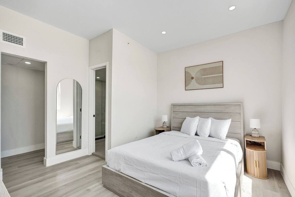 A modern bedroom with a large bed, a wooden headboard, a nightstand with a lamp, and a painting on the wall.
