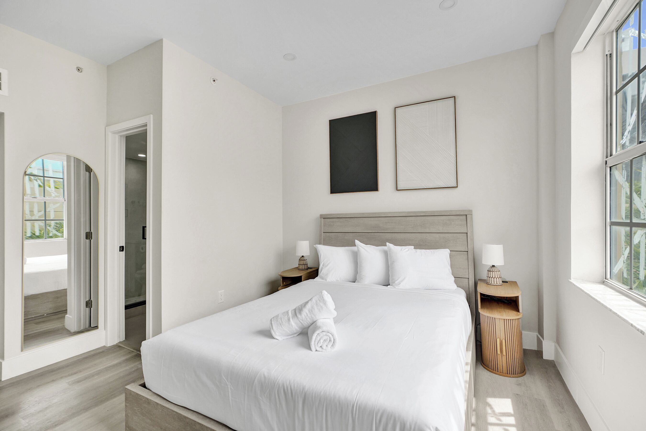A modern bedroom with a large bed, two bedside tables, a window, and a door leading to a bathroom.