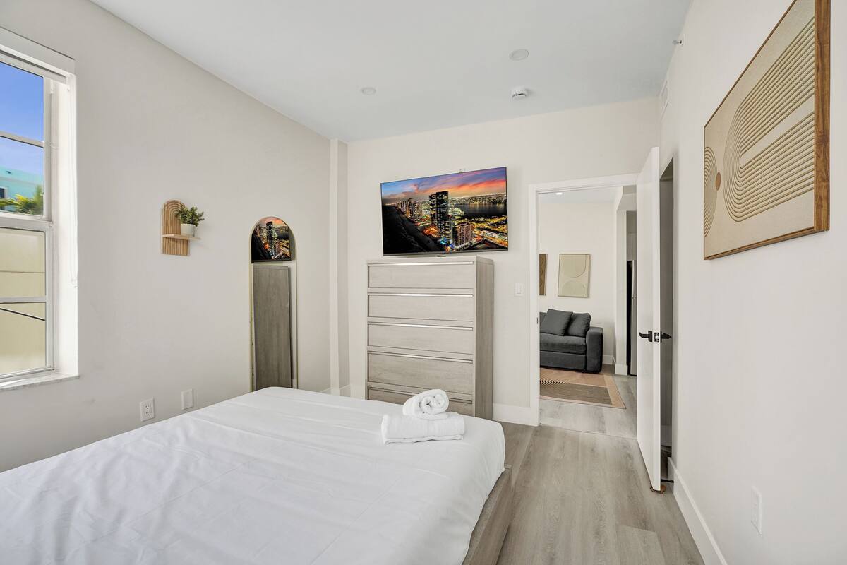 A bedroom with a bed, a dresser, a mirror, and a painting on the wall.