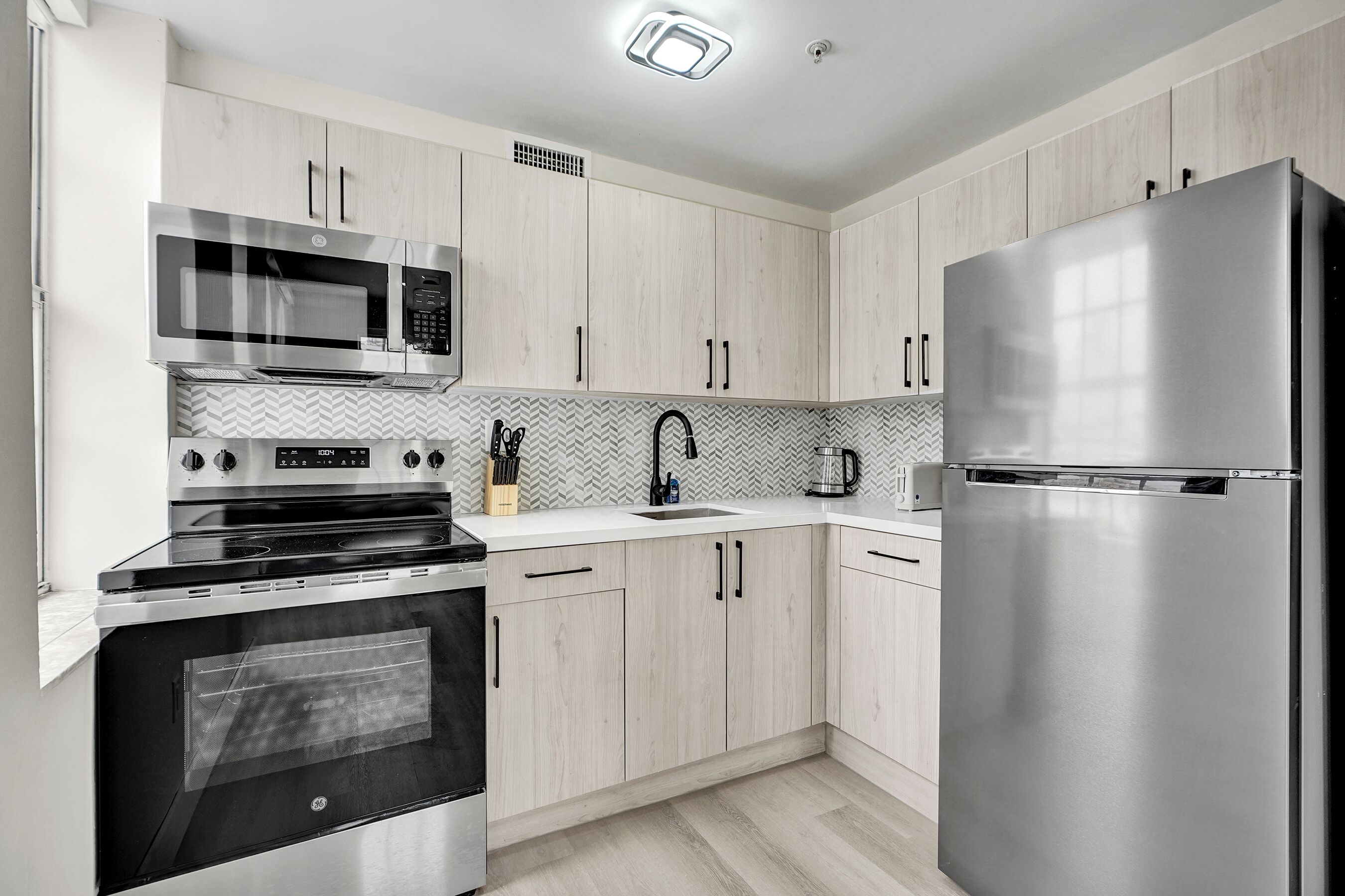 A modern kitchen with stainless steel appliances, wooden cabinets, and a herringbone-patterned backsplash.