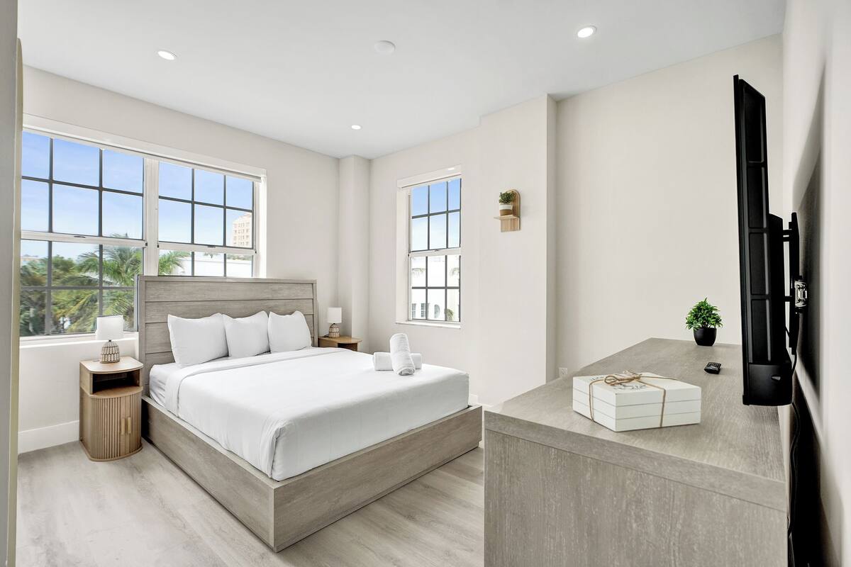 A modern bedroom with a large bed, bedside tables, a flat-screen TV, and a small plant.