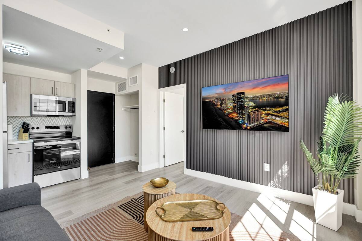 A modern kitchen with built-in appliances, a dining area with a round wooden table, and a large cityscape painting on the wall.