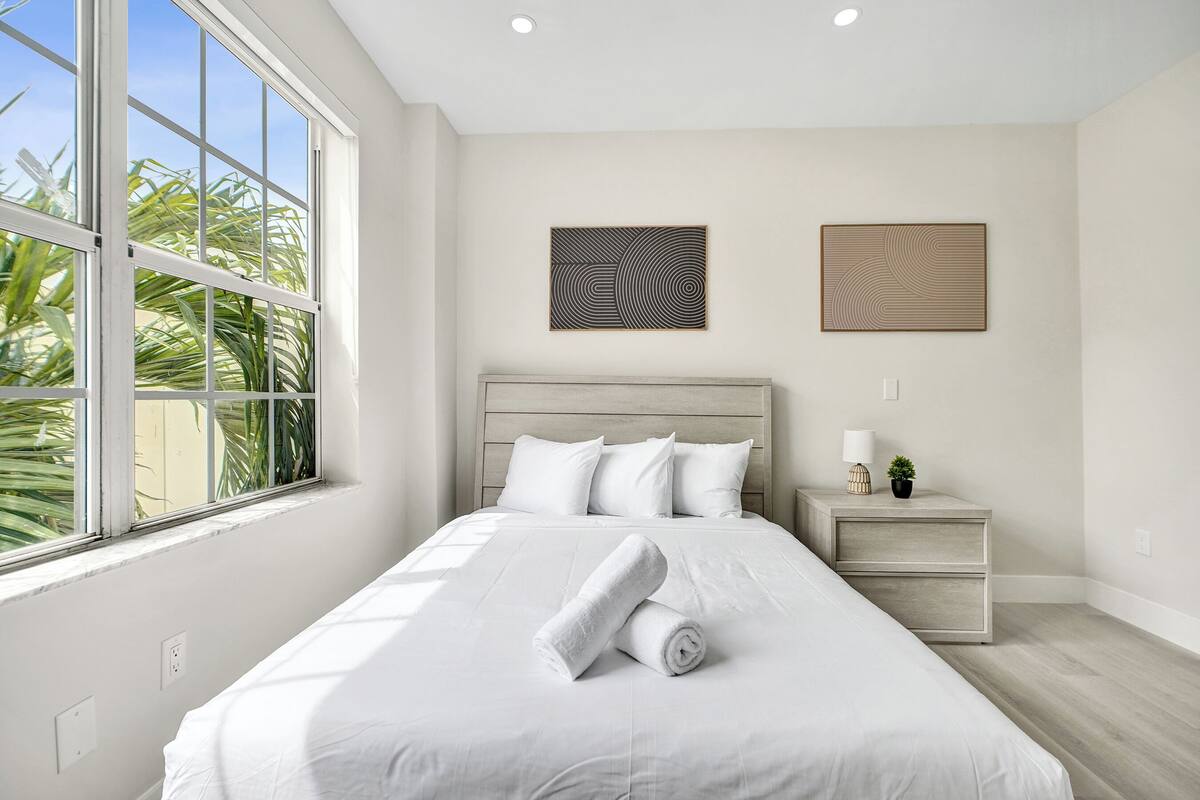 A neatly arranged bedroom with a large bed, a nightstand, and two wall-mounted artworks.