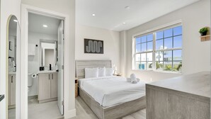 A modern bedroom with a large bed, a bathroom with a toilet and sink, and a window with a view. - SoBe Suites 727 (Miami Beach)