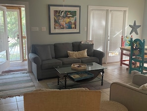 Ein Wohnzimmer mit grauem Sofa, einem Glastisch, einem gerahmten Gemälde und einer Stern-Dekoration an der Wand.