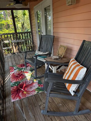 Eine hölzerne Veranda mit zwei Schaukelstühlen, einem kleinen Tisch und einem Blumenteppich.
