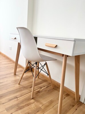 Ein weißer Schreibtisch mit einem Holzstuhl, einer Schublade und einem kleinen Holzgriff.