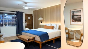 Habitación de hotel con cama, mesita de noche, silla y vistas a la ciudad a través del ventanal.