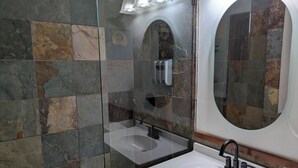 Un baño con cabina de ducha de vidrio, un lavabo blanco con grifo negro y un espejo con marco ovalado.