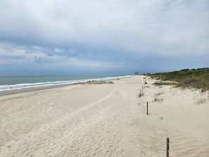 Ein Strand mit einem Sandweg, Meereswellen und einem Gebäude in der Ferne.
