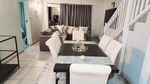 A dining area with a table set for four, a sofa, and a staircase. - Luxury Apartment in Waikiki E5 Close to the Beach (Ballito)
