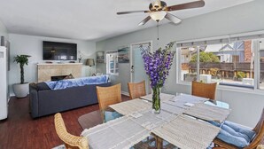 A modern living room with a sofa, dining table, chairs, a ceiling fan, and a TV. - 3bed 2bath beach cottage Steps to the Sand in MB (San Diego)