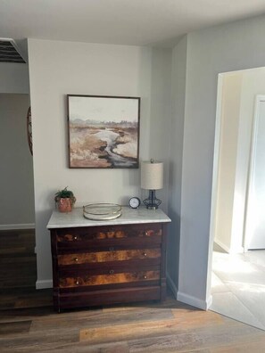 Una habitación de esquina con un aparador de madera, un cuadro en la pared, una lámpara y un reloj.