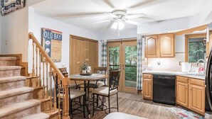 A kitchen with wooden cabinets, a dining table with chairs, a ceiling fan, and a staircase. - Spacious A-Frame Family Beach Getaway - Sleeps 8 (Ocean Pines)