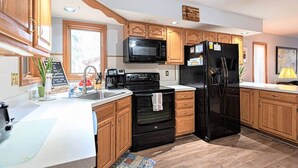 A modern kitchen with wooden cabinets, a black refrigerator, a microwave, a stove, and a sink. - Spacious A-Frame Family Beach Getaway - Sleeps 8 (Ocean Pines)
